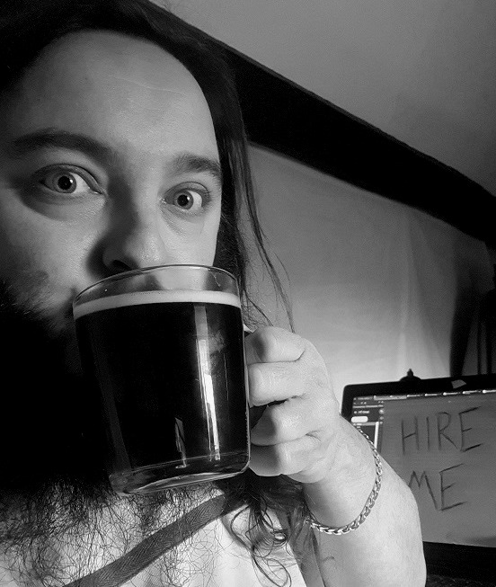 A photo of a long-haired man about to drink a cup of black coffee at his desk.