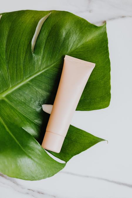 Cream tube on a fresh green leaf against a marble surface, embracing natural beauty themes.