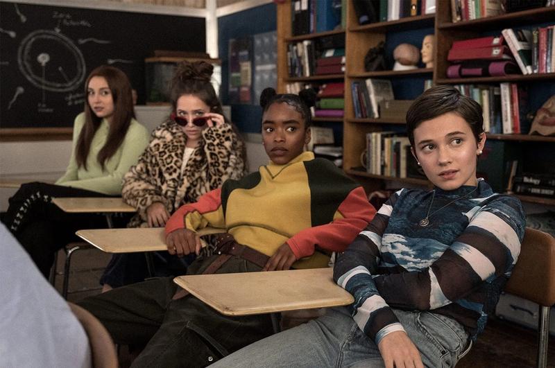 Four women sit at individual desks in the back of a classroom