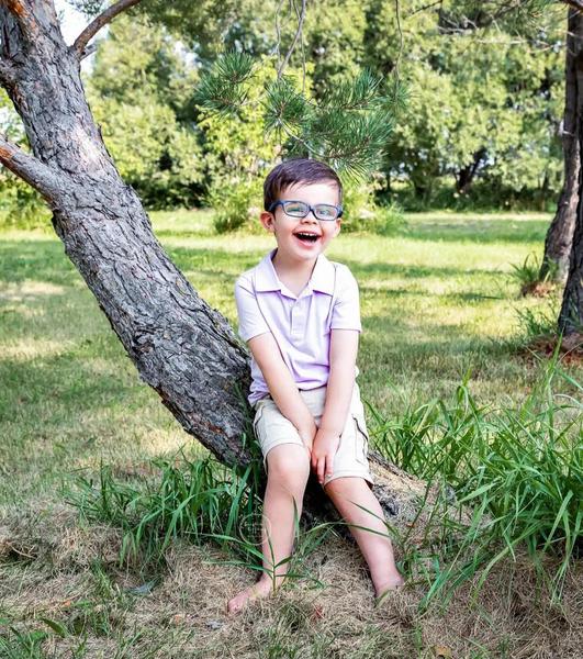 Picture of four-year-old Oaklin Piec, sitting on a tree in a forested area. Oaklin was diagnosed with a rare condition that will cause him to go blind.