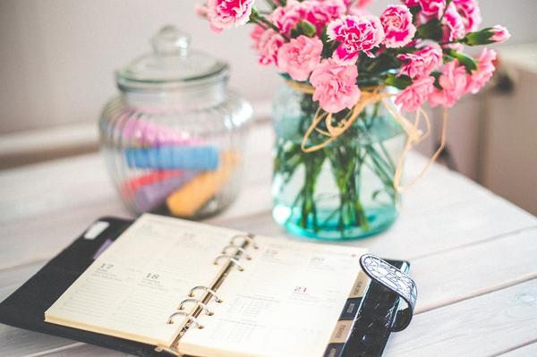 Open schedule book and flowers on a desk, representing creative storytelling and branding for small businesses being an important part of the schedule.