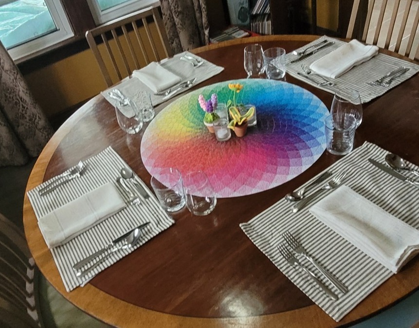Dining table set for dinner with rainbow puzzle and crotched flowers as the centrepiece.