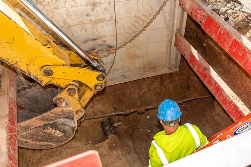 A construction worker in a hole being dug out by a loader truck