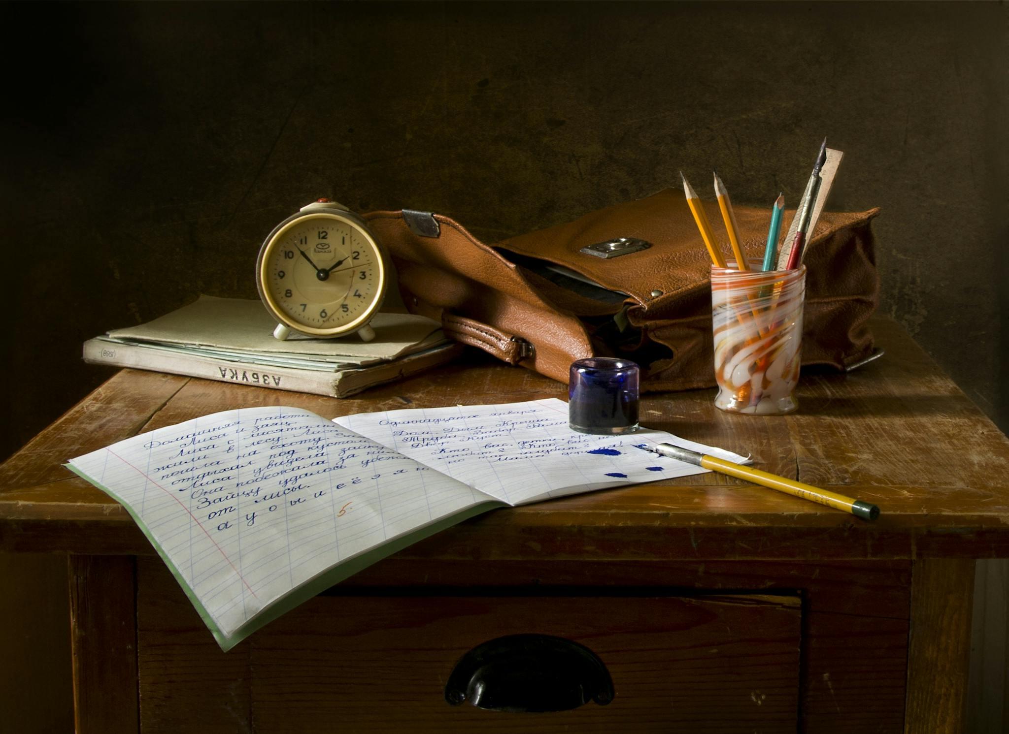 A wooden desk with a clock, notebook, and writing utensils