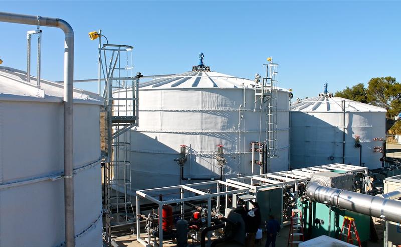 Three large white holding tanks connected through a complex series of pipes