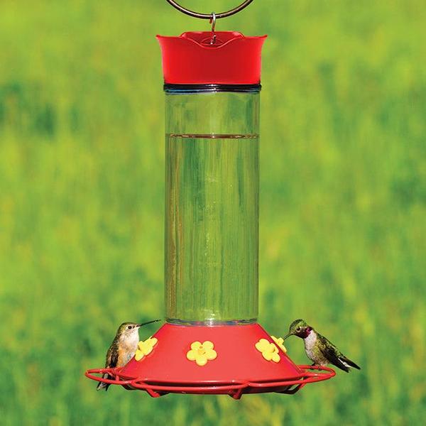 Several hummingbirds are perched on a tall, hanging red hummingbird feeder, sipping nectar from the yellow feeding ports.