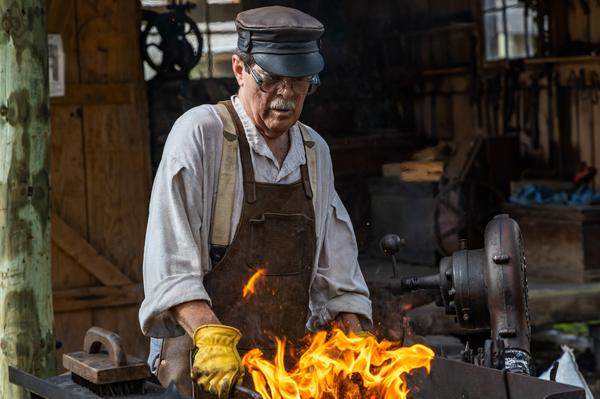 A blacksmith works on a project over an open coal forge