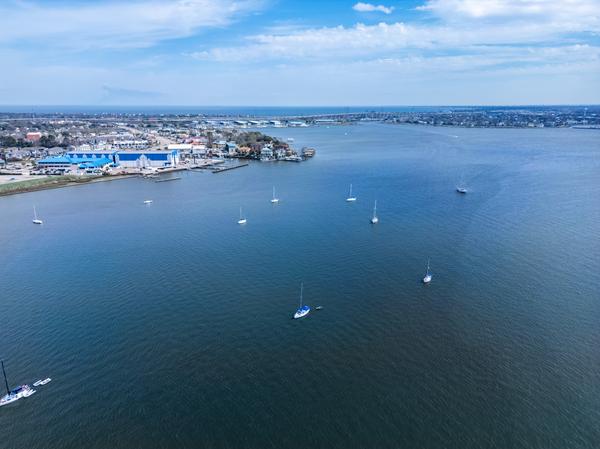 Aerial view of Clear Lake with sailboats scattered across the water and a shoreline featuring marinas and waterfront buildings under a partly cloudy sky.