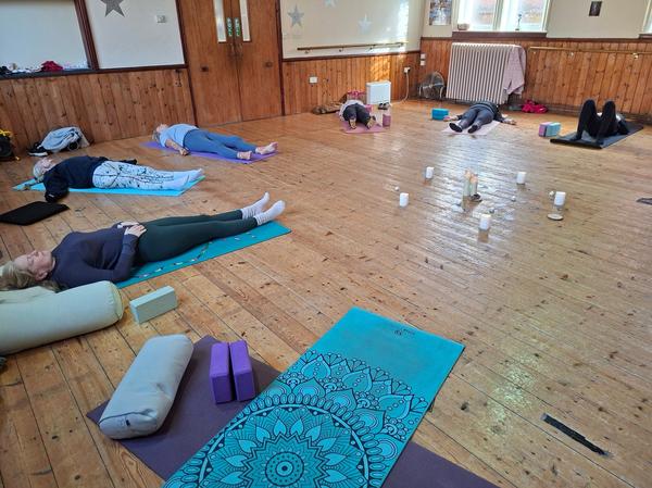 Students practicing Savasana relaxation at a Daisy Chain Yoga class, featuring bolsters, blocks, and a candlelit center.