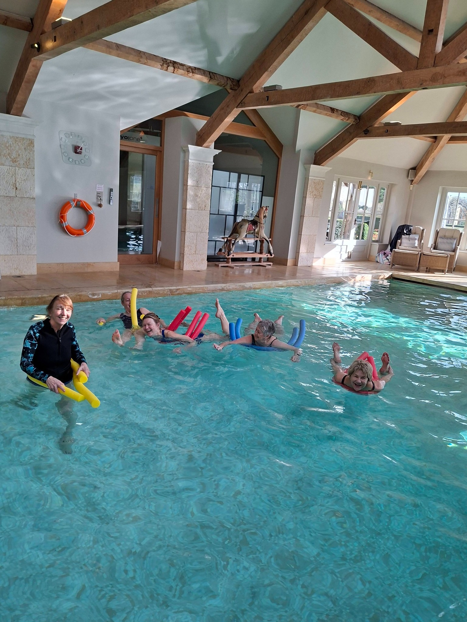 Aqua Yoga class at Honington Grange, Grantham, featuring students using pool noodles for low-impact water exercise and relaxation.