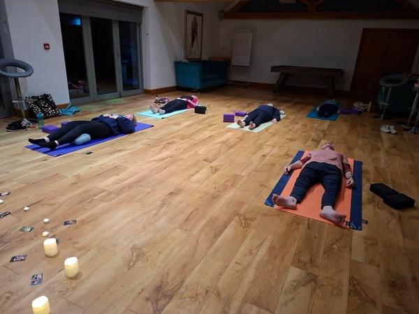 Yoga students practicing Savasana (corpse pose) for relaxation in a candlelit studio at Daisy Chain Yoga.