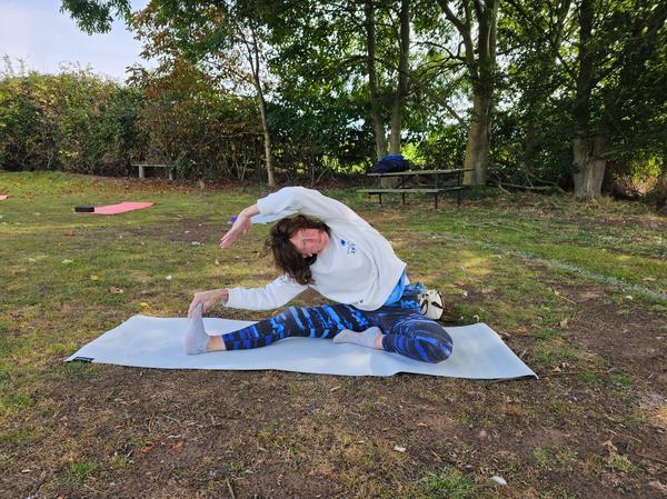 Yoga instructor Rachel Metcalfe of Daisy Chain Yoga practicing a seated side stretch (Parsva Upavistha Konasana) on a mat during an outdoor yoga session.