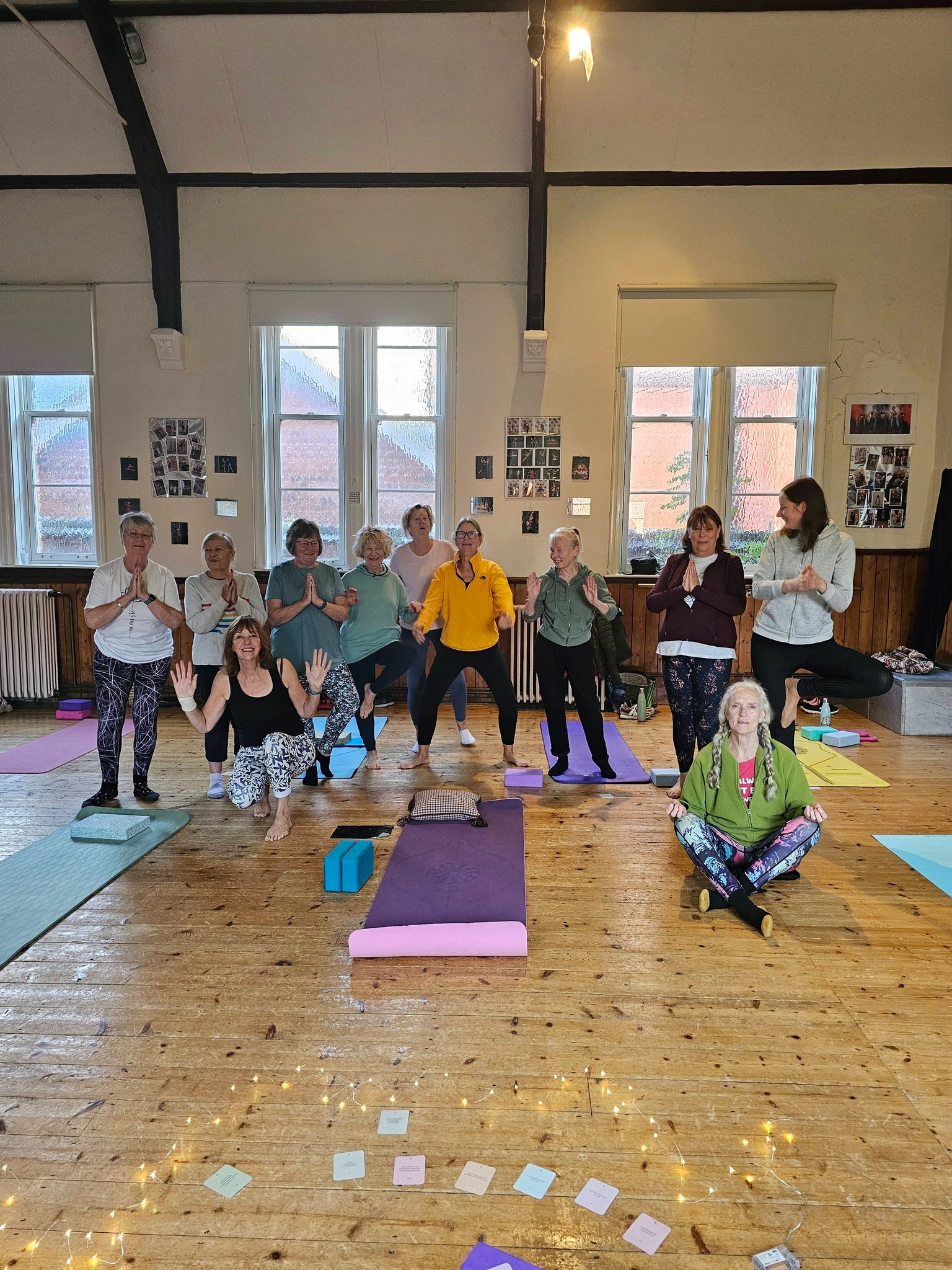 A welcoming community yoga class at Swayfield Village Hall, featuring a group of students practicing tree pose and meditation on colorful mats.