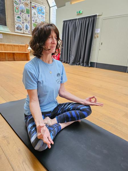 Yoga instructor Rachel Metcalfe of Daisy Chain Yoga practicing seated meditation in a peaceful community hall.
