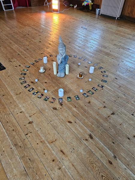 A meditative center circle at Daisy Chain Yoga featuring a Buddha statue, white candles, and oracle cards on a wooden floor.
