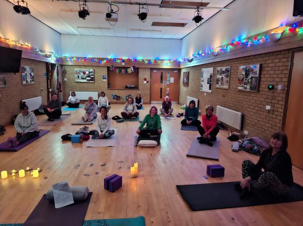 A welcoming mixed yoga class at Swayfield Village Hall with Daisy Chain Yoga, featuring students on mats in a brightly lit community space.