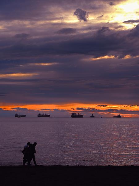 People walking across English Bay Beach during golden hour