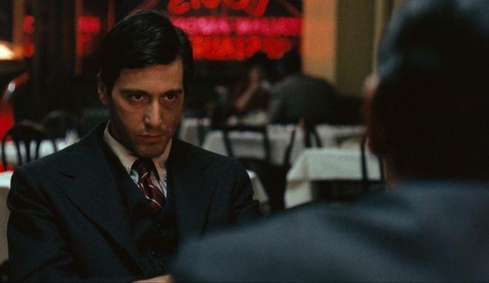 Man in a dark suit seated at a restaurant table, looking at the person across from him