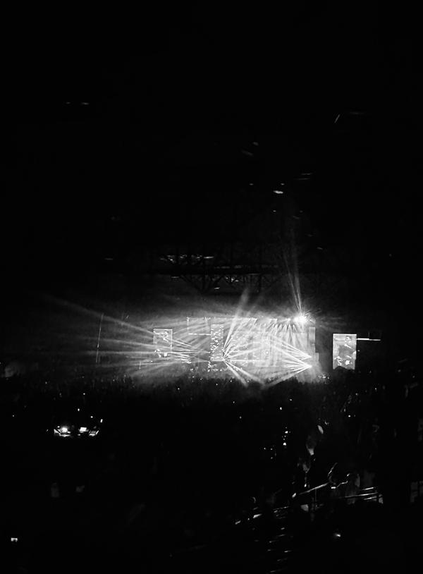Concert stage lit up with beams of light, seen from a dark crowd