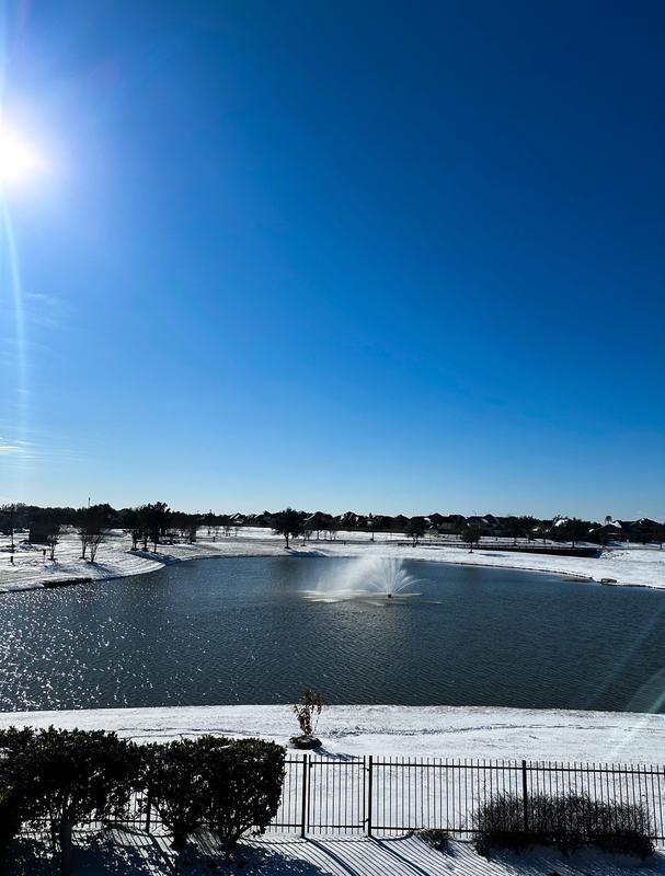 Pond fountain surrounded by snow-covered banks under a bright blue sky