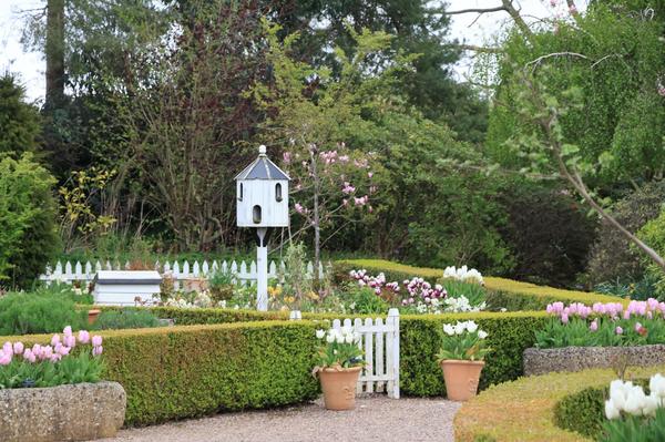 An English garden with a small white house-shaped birdhouse among the plants.