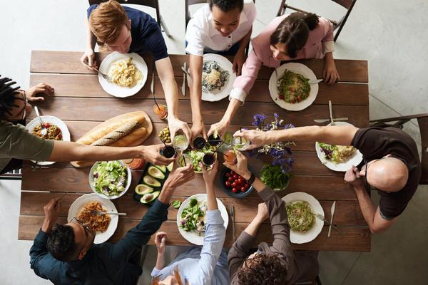 A group of people clinking glasses over a dinner table. A group of people clinking glasses over a dinner table.