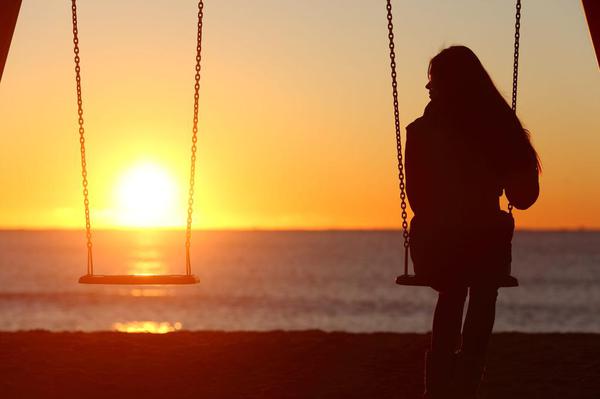 Woman sitting on a swing at the beach watching a sunset Woman sitting on a swing at the beach watching a sunset