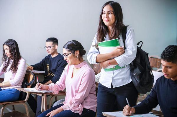 A student standing up in class, holding a notebook to her chest.