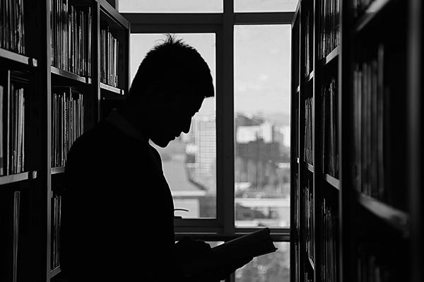 A silhouette of a man reading between two tall bookshelves A silhouette of a man reading between two tall bookshelves