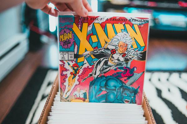 Someone pulling an X-Men comic with Storm and Beast on the cover from a cardboard box full of comics Someone pulling an X-Men comic with Storm and Beast on the cover from a cardboard box full of comics
