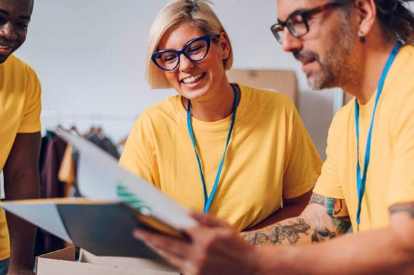 Three people in yellow T-shirts wearing blue lanyards and holding pieces of paper Three people in yellow T-shirts wearing blue lanyards and holding pieces of paper
