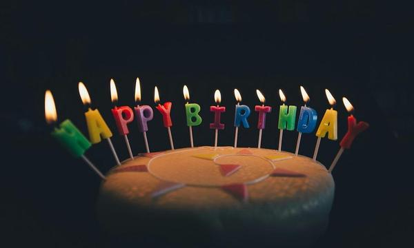 A birthday cake in a dark room, lit candles spelling "Happy birthday"