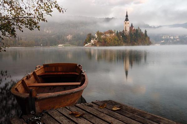 A small wooden boat moored at a dock on a lake, with a castle looming on a distant island.