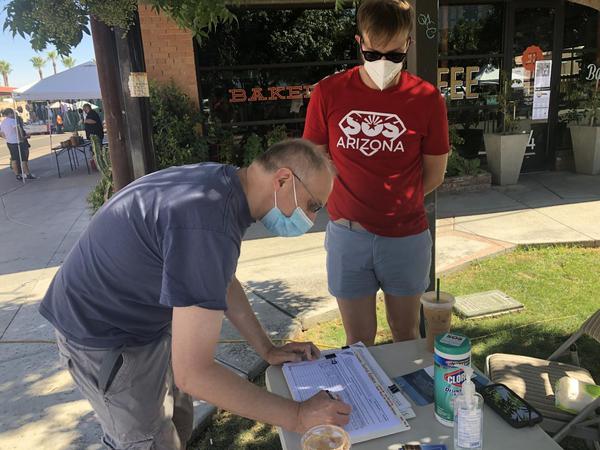A voter signs a petition for a criminal justice reform initiative during a signature gathering event at the downtown Phoenix farmer's market, June 20, 2020.