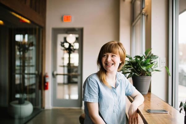 Person sitting at a tabletop next to a plant smiling behind them